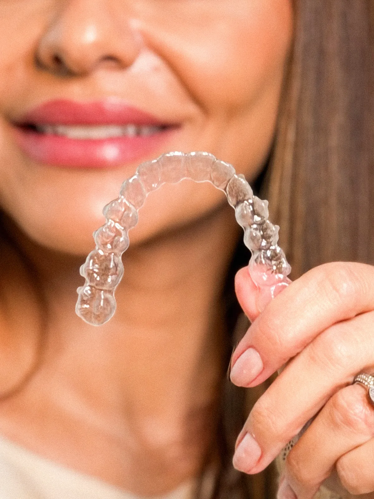 Mão segurando um alinhador transparente em frente a um sorriso