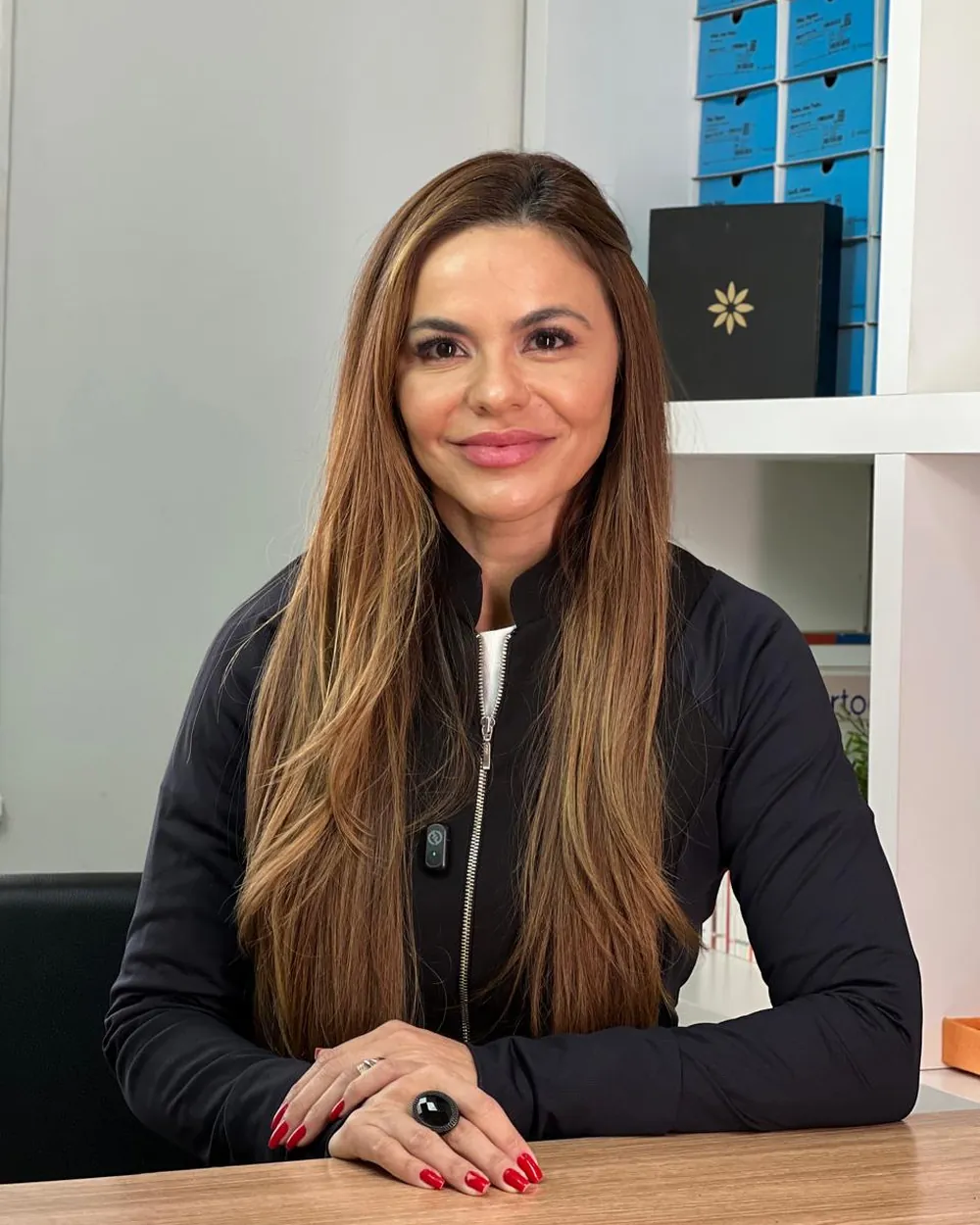 Dra. Lídia Scatulino, especialista em Harmonização Orofacial, sentada à mesa do consultório da OrthoVip