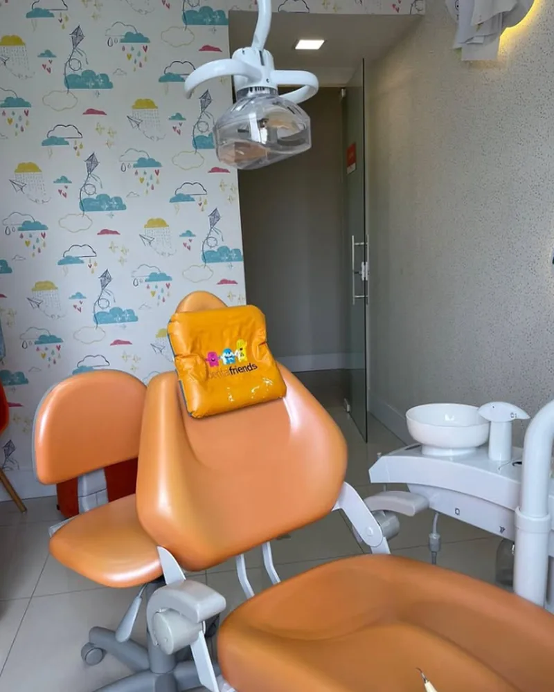 Consultório infantil com cadeira odontológica laranja e papel de parede de nuvens
