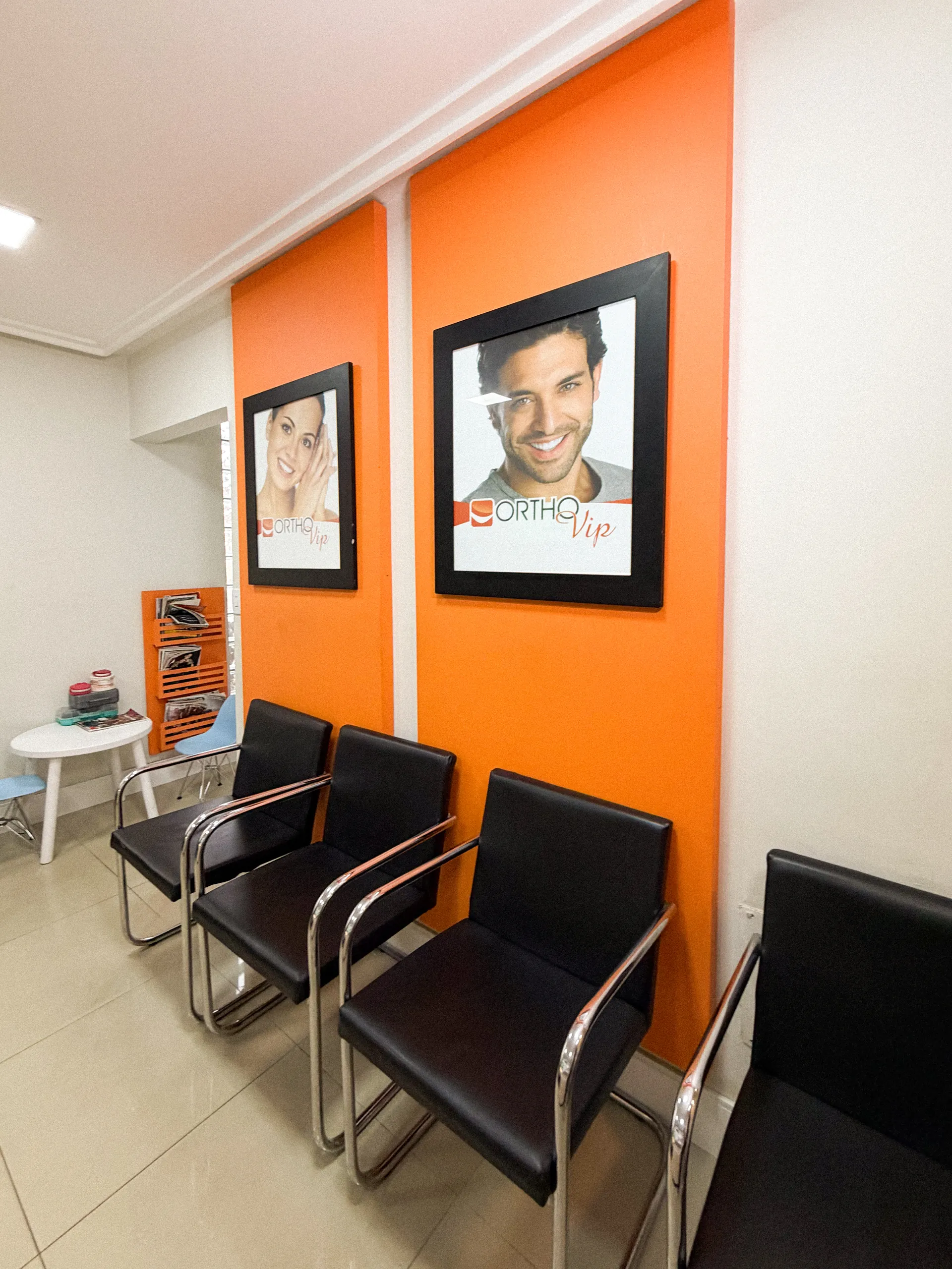 Recepção da OrthoVip com parede laranja, cadeiras pretas e quadros de sorrisos