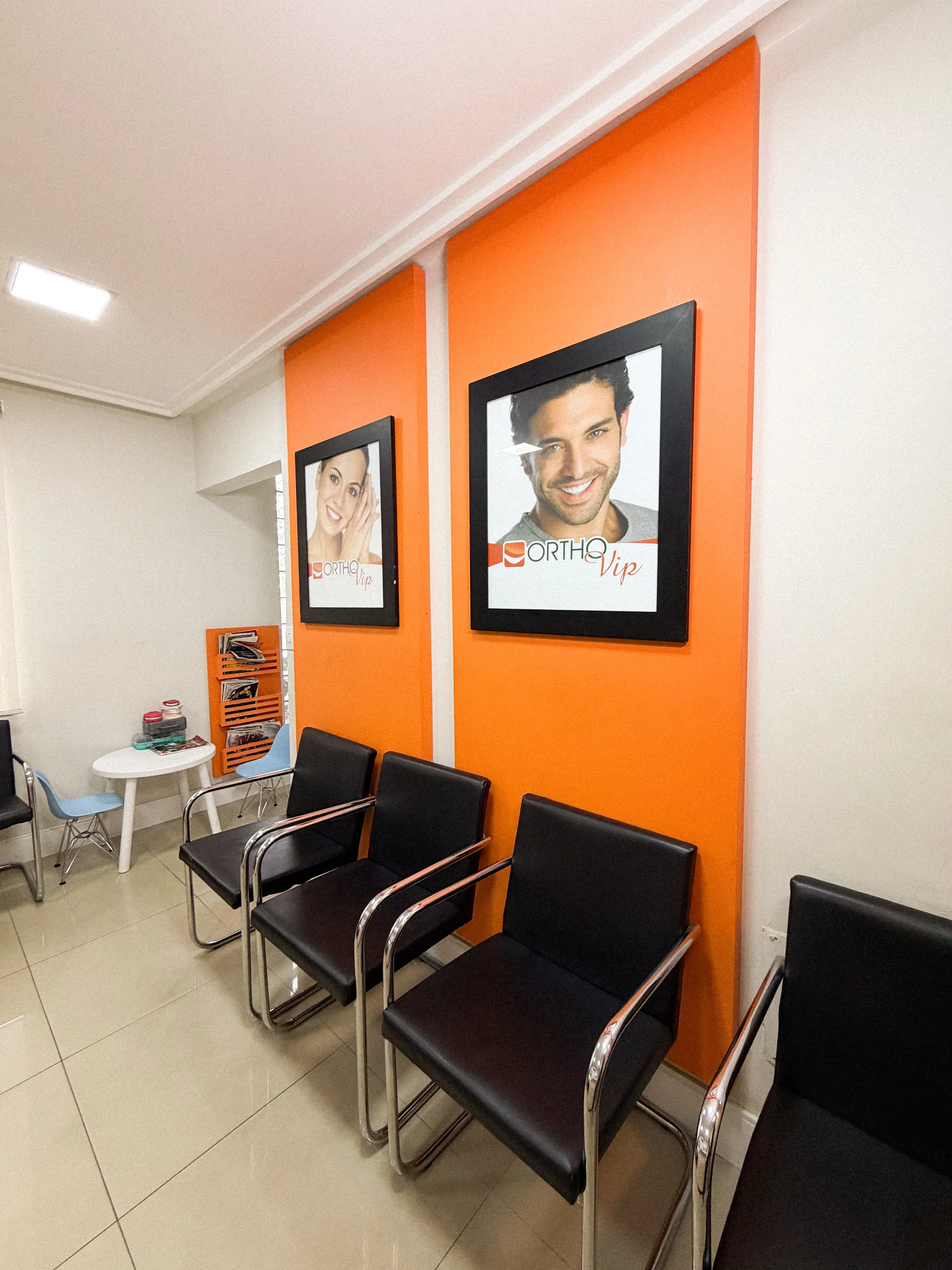 Sala de espera da OrthoVip com parede laranja e quadros de sorrisos